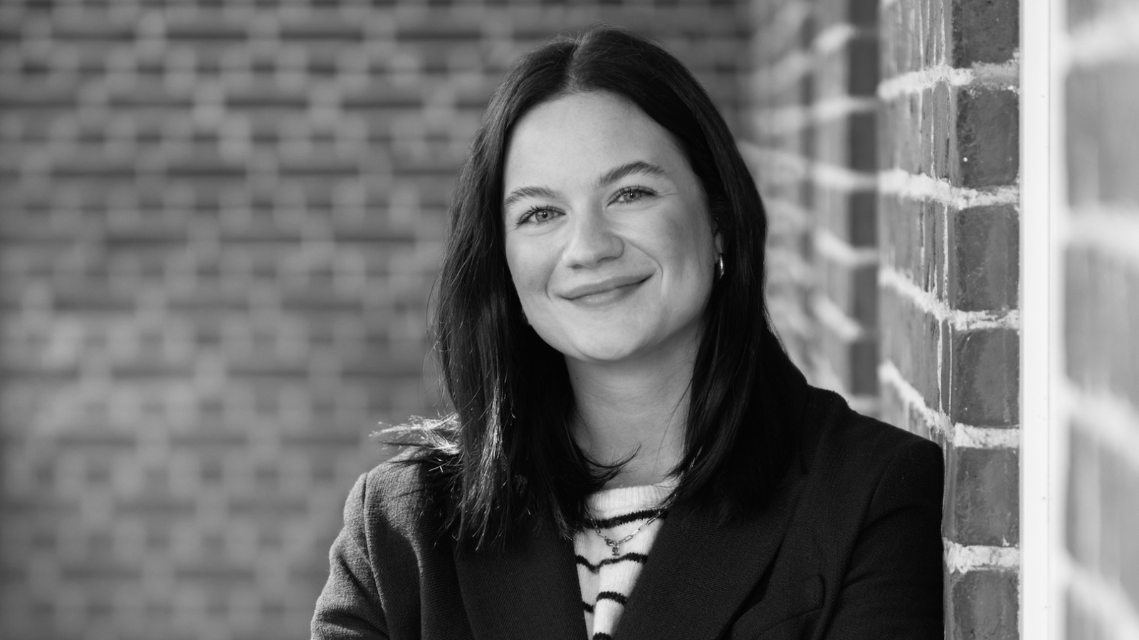 A woman is standing in front of a brick wall and smiling at the camera